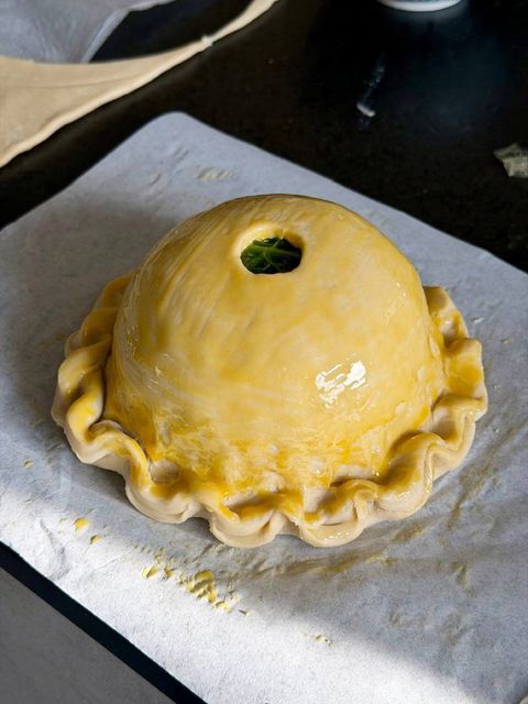 Glazed game pithiviers before baking, with crimped puff pastry edges and a central chimney
