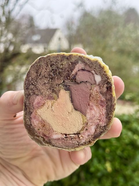 A slice of the hare ballotine held up, showing the foie gras and saddle set in the shredded hare and farce