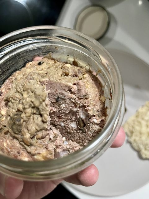 An opened jar of pigeon pâté showing a coarse cross-section, with a cracker alongside