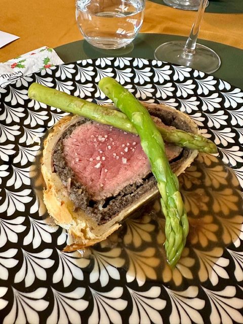 Plated slice of beef Wellington with green asparagus and sauce